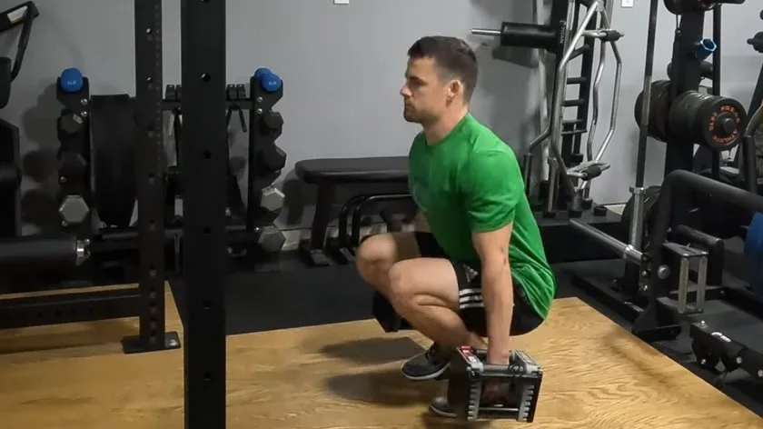 Coach Brian demonstrating a deep squat hold with dumbbells in his home gym